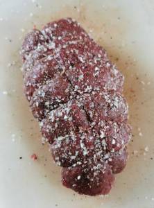 Helstekt rostbiff som är täckt med salt och peppar på en vit tallrik.