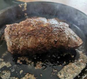 Helstekt rostbiff som ligger i en stekpanna med fett och ånga runtom.