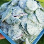 En skål med gurksallad som innehåller skivade gurkor och dill i en krämig sås.