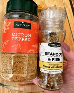 Två kryddburkar, en med citronpeppar och en med skaldjurskrydda, hålls i en hand.