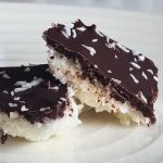 Två kokosbitar med chokladöverdrag och kokosflingor på en tallrik.