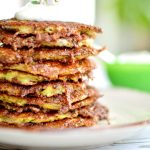 En hög av zucchinifritters med en klick gräddfil och en ört på toppen.