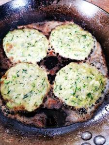 Fyra zucchinifritters som steks i en panna med bubblande olja.