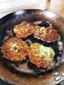 Fyra zucchini-fritters som steks i en panna med smör.