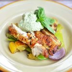 Knappert stekt kycklingstek serverad med grönsaker och en grön sås på en tallrik.