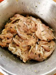 Marinerade kycklingbitar i en metallskål med örter och kryddor.