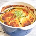 Zucchinigratäng med gyllenbrun yta och färska örter på toppen i en ugnsform.