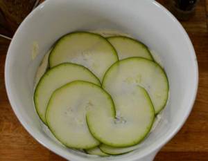 Skivor av zucchini placerade i en vit skål med en krämig blandning.