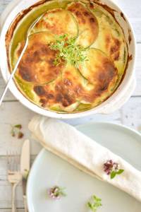 Zucchinigratäng med gyllenbrun yta i en vit ugnsform, dekorerad med färska örter.