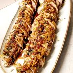 Sliced double-marinated pork tenderloin arranged on a serving platter with a glaze.