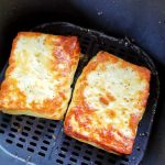 Två bitar grillad halloumi i en airfryer med gyllene yta.