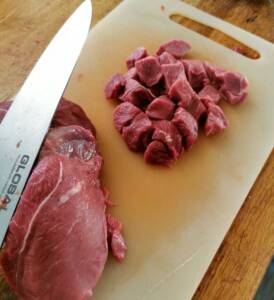 Skärbräda med bitar av kött och en kniv liggande bredvid.