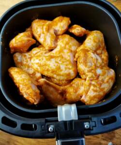 Kycklingvingar täckta med marinad i en airfryer innan tillagning.