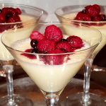 Tre glas med pannacotta toppad med hallon och blåbär på en silverbricka.