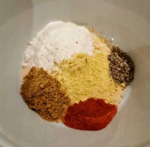 En blandning av olika kryddor i en skål, inklusive vitlökspulver, ingefära och paprika.