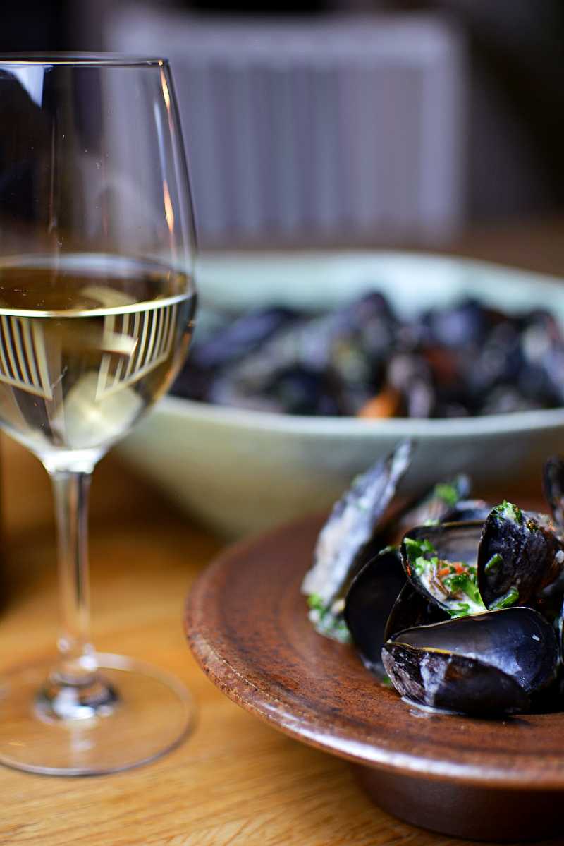 Moules Marinières 8 Moules Marinières, eller vinkokta blåmusslor i en skål och ett glas vitt vin bredvid.