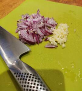 Hackad rödlök och vitlök placerad på en grön skärbräda med en kniv.