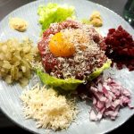 En tallrik med tartar, äggula, riven ost och grönsaker som lök och rödbetor.