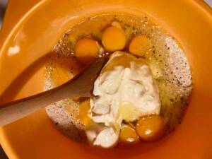 En orange skål med ägg, gräddfil och kryddor blandade med en träsked.