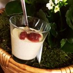 Kanelpannacotta serverad i ett glas med bär på toppen, placerad i en korg med gröna växter.