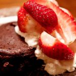 Chokladfondant toppad med grädde och skivade jordgubbar på en tallrik.