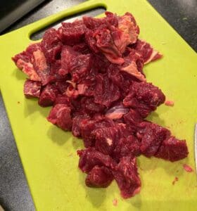 Köttbitar av olika storlekar på en grön skärbräda i ett kök.