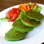 Fyra spenatbiffar på en tallrik med grönsaker som tomat, morot och sallad.