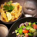 Friterad svartfisk serverad med limeklyftor och en skål med sallad och sås.