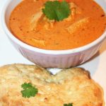 Skål med kyckling tikka masala och naanbröd på en vit bakgrund.