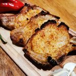 Tre grillade kotletter placerade på en skärbräda med vitlök och chili.