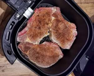 Tre kryddade köttbitar placerade i en airfryer med svart insida.