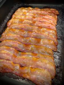 En plåt med flera skivor stekt bacon som ligger i rad.