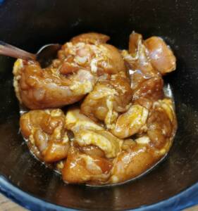 Marinerade kycklingbitar i en svart skål med en träsked.