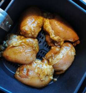 Marinerade kycklinglår placerade i en air fryer innan tillagning.