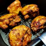 Flera kycklinglårfiléer som tillagas i en airfryer med en gyllenbrun yta.