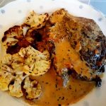 En tallrik med en köttbit i sås och rostad blomkål på sidan.