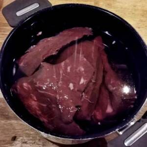 Köttbitar som ligger i en kastrull med vatten, delvis nedsänkta.