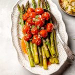 Grön sparris och körsbärstomater serverade på en vit tallrik med en sked.