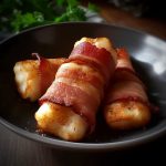 Tre bitar halloumi inlindade i bacon på en svart tallrik.