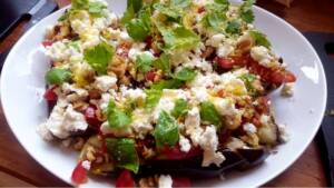 En tallrik med aubergine toppad med fetaost, valnötter och färska örter.