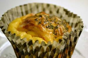 Matmuffins i en pappersform med fetaost och soltorkade tomater, dekorerad med örter.