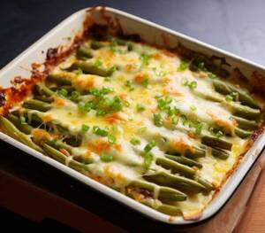 En ugnsform med gratinerade haricots verts täckta med smält ost och grön lök.