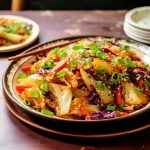 En tallrik asiatisk kalwok med grönsaker som kål, paprika och sesamfrön, garnerad med hackad grön lök.