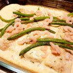 Parmesangratinerad torskfilé med räkor och gröna bönor i en ugnsform.
