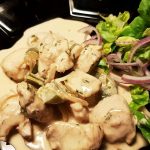 En tallrik med julkyckling i sås, serverad med grönsallad och rödlök.