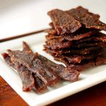 En hög med biffjerky som ligger på en vit tallrik med några bitar bredvid.