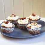 Fem hasselnötsmuffins med grädde och hackade nötter på toppen, placerade på en tallrik.