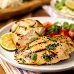 Två grillade kycklingfiléer med lime och färska örter på en tallrik.