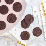 Runda chokladplattor av mörk choklad på en rosa tallrik med några plattor på bordet.
