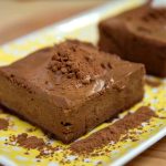 Två bitar chokladbrownie på en tallrik med kakaopulver runtom.